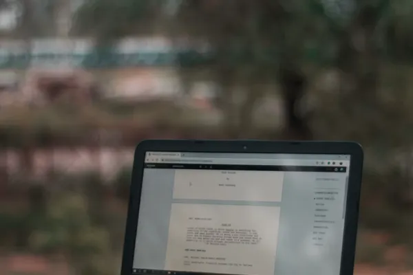An open laptop showing screenwriting software, with a spiral notebook on the keyboard, on a stone ledge outdoors.