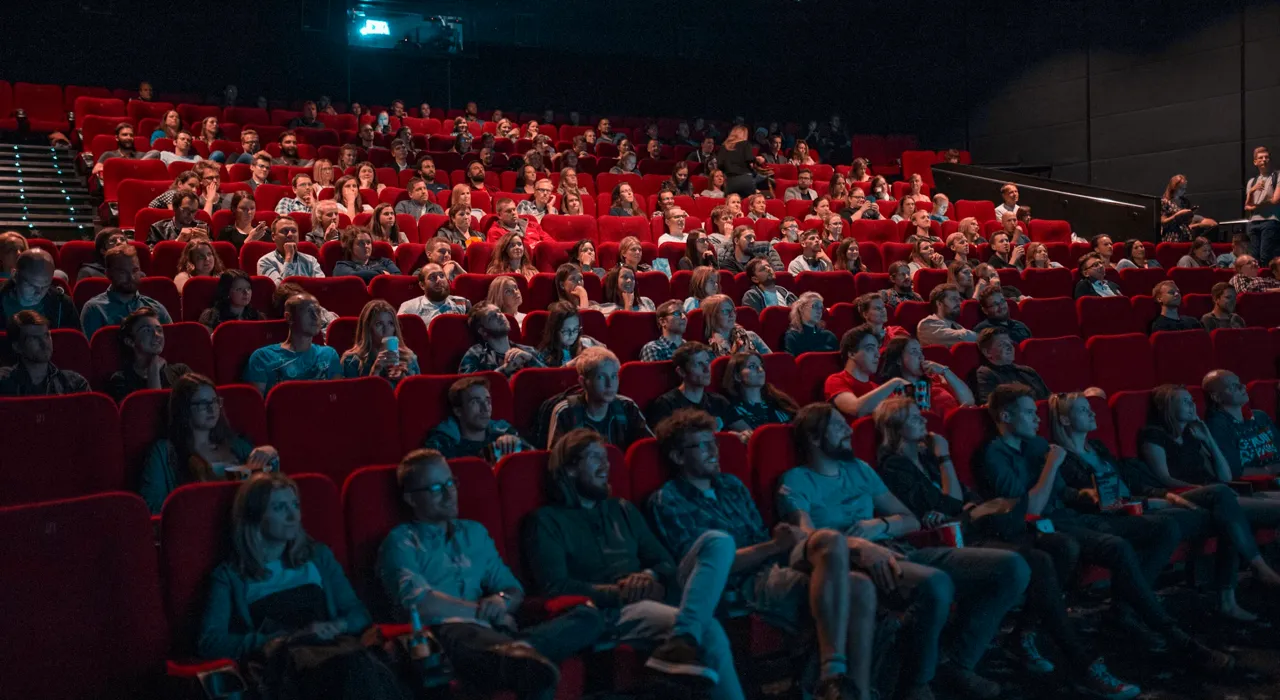 A full movie theater with red seats, the audience lit by the screen.