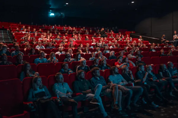 A full movie theater with red seats, the audience lit by the screen.